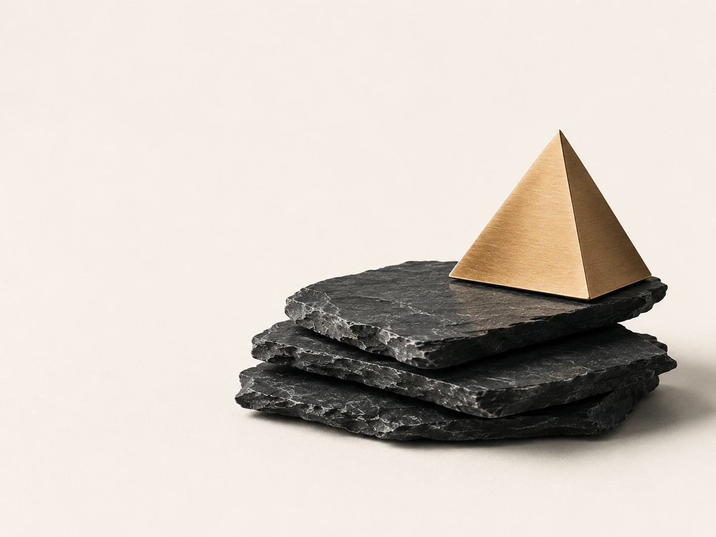 Stacked dark slate slabs supporting a brushed bronze pyramid on a warm neutral background — the Slate and Summit brand mark for financial clarity